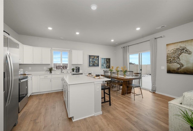 kitchen featuring visible vents, a breakfast bar, a center island, appliances with stainless steel finishes, and light wood finished floors