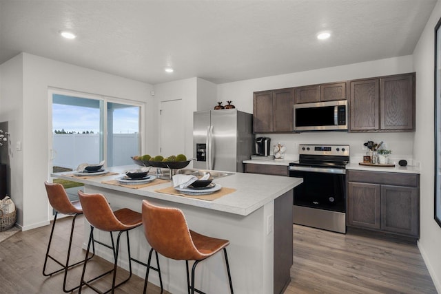 kitchen with light countertops, dark brown cabinets, appliances with stainless steel finishes, a kitchen breakfast bar, and light wood-type flooring