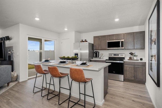 kitchen featuring a kitchen bar, light wood finished floors, a center island, appliances with stainless steel finishes, and light countertops