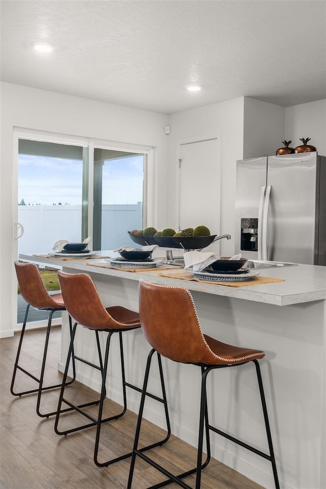 kitchen with stainless steel fridge, light countertops, a kitchen bar, and light wood-style floors