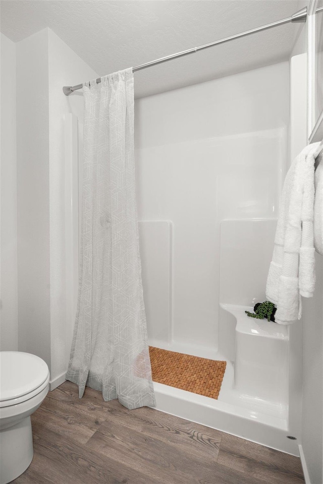 full bath featuring a shower stall, toilet, baseboards, and wood finished floors