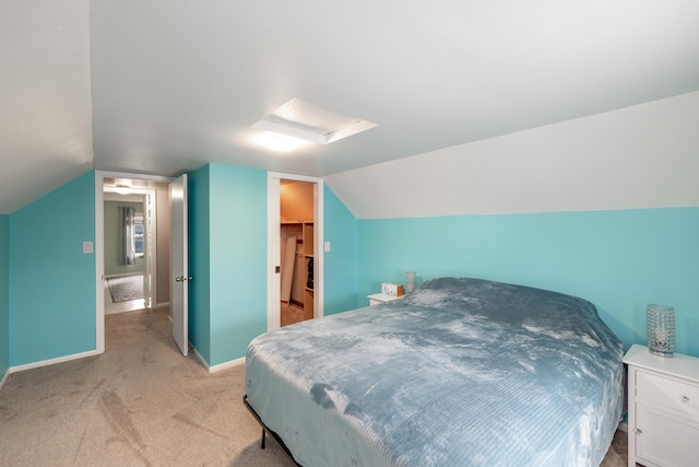 bedroom with baseboards, attic access, lofted ceiling, a walk in closet, and light colored carpet