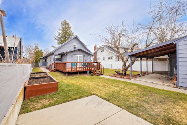 rear view of property featuring a wooden deck, fence private yard, a yard, a garden, and a carport