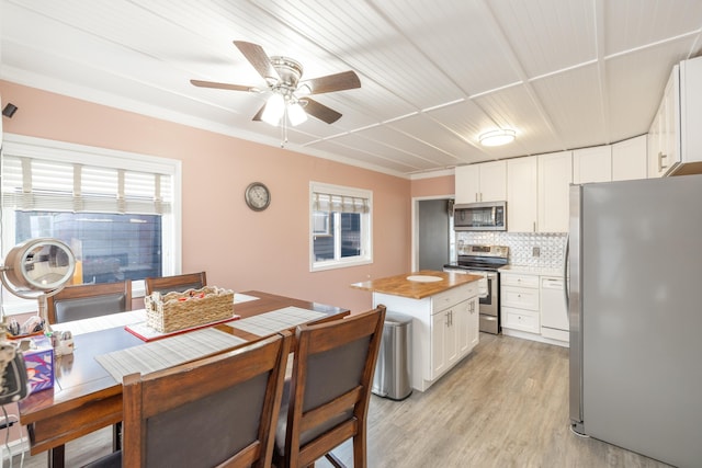 kitchen featuring light wood finished floors, a kitchen island, decorative backsplash, white cabinets, and appliances with stainless steel finishes