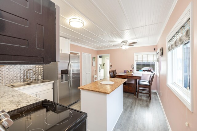 kitchen with stainless steel refrigerator with ice dispenser, a sink, wood counters, black / electric stove, and white cabinets