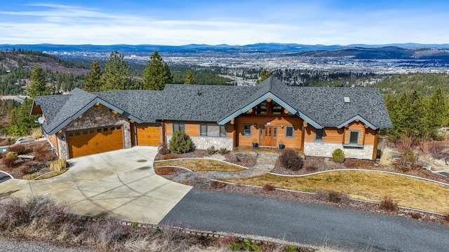 view of front of property with stone siding, a mountain view, an attached garage, and a shingled roof