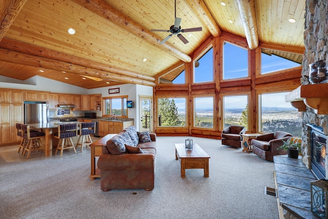 living area with ceiling fan, beamed ceiling, wood ceiling, a stone fireplace, and high vaulted ceiling