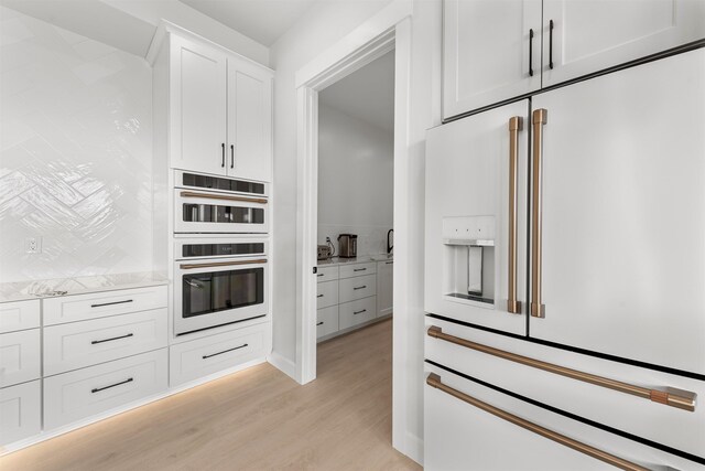 kitchen with light wood-type flooring, white appliances, white cabinets, and light stone countertops