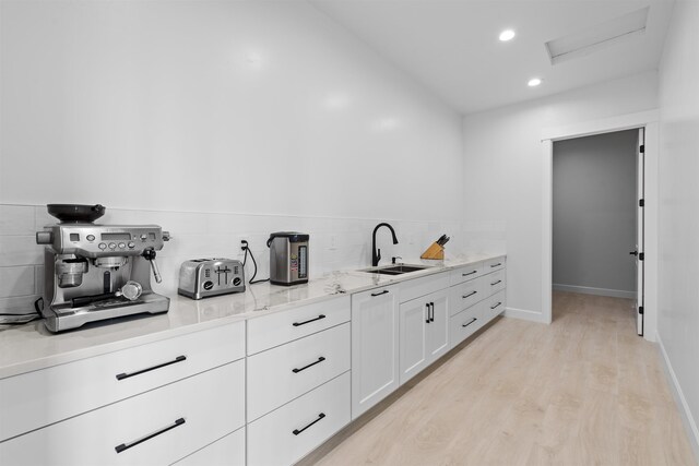 kitchen with tasteful backsplash, light stone countertops, light wood-style floors, white cabinets, and a sink