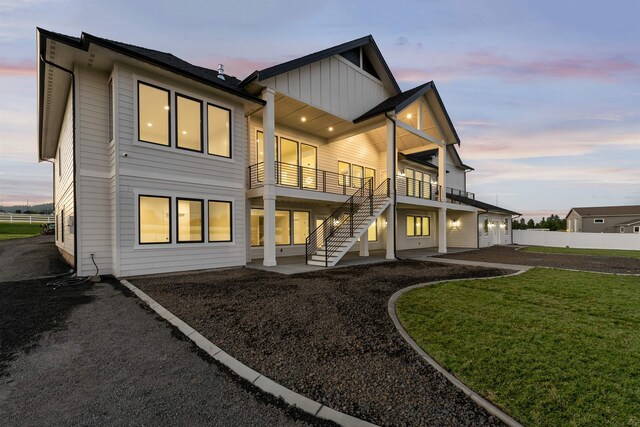 back of property at dusk with a lawn, fence, board and batten siding, a balcony, and a patio area