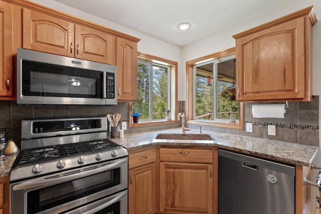 kitchen featuring a sink, decorative backsplash, light stone counters, and stainless steel appliances