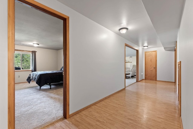 corridor with baseboards, light carpet, and light wood finished floors