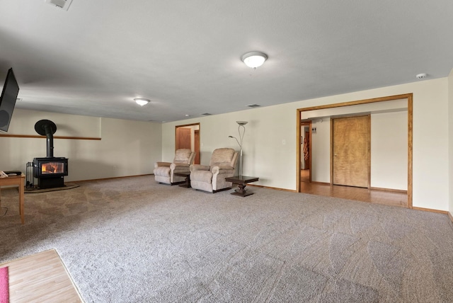 living area with a wood stove, carpet, visible vents, and baseboards