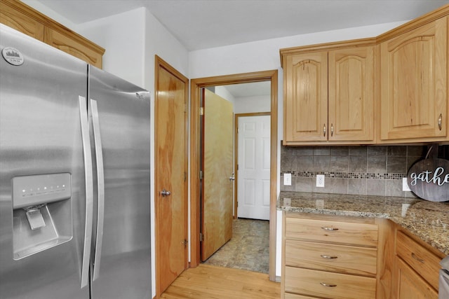 kitchen with light stone countertops, light brown cabinets, light wood finished floors, stainless steel fridge, and backsplash