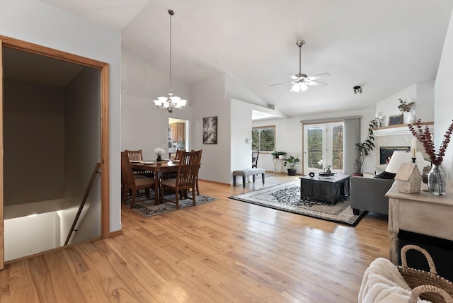 living area featuring light wood-style floors, a glass covered fireplace, high vaulted ceiling, and ceiling fan with notable chandelier