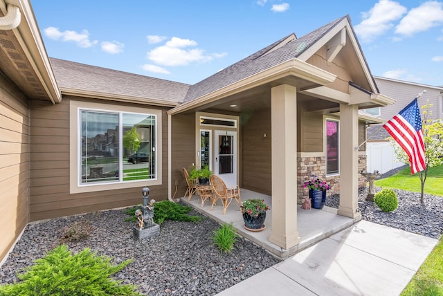 doorway to property featuring stone siding and a shingled roof