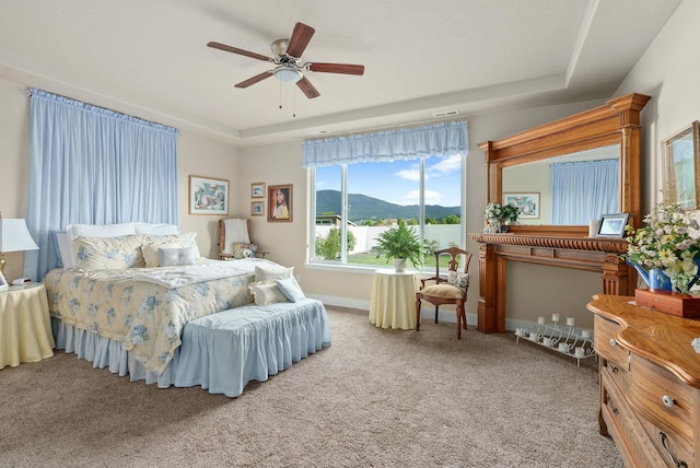 bedroom featuring baseboards, a tray ceiling, carpet floors, a mountain view, and a ceiling fan