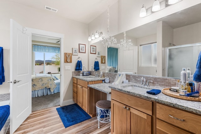 ensuite bathroom featuring visible vents, a stall shower, a sink, wood finished floors, and decorative backsplash