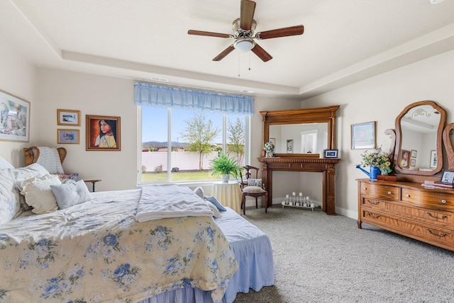 carpeted bedroom with baseboards, a raised ceiling, and a ceiling fan