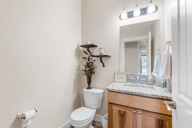 bathroom featuring vanity, toilet, baseboards, and tasteful backsplash