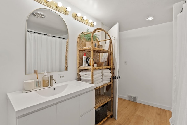 bathroom with visible vents, vanity, baseboards, and wood finished floors