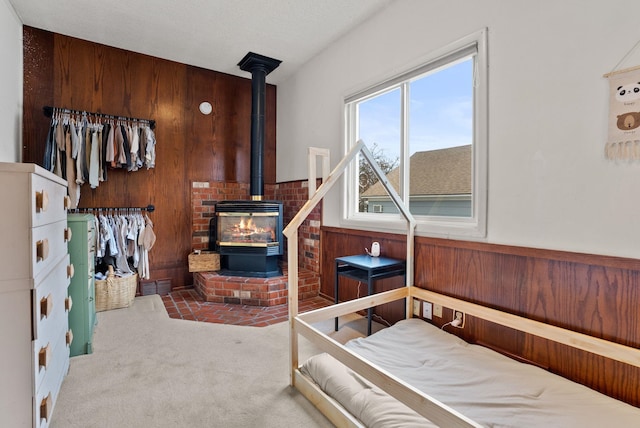 carpeted bedroom featuring wooden walls, wainscoting, and a wood stove