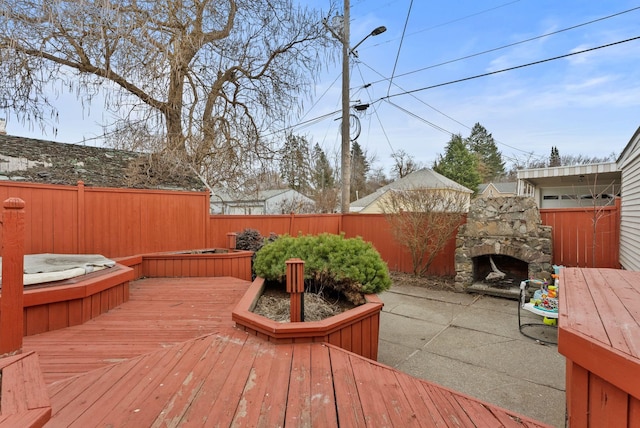 wooden deck featuring a hot tub, an outdoor stone fireplace, a patio, and fence