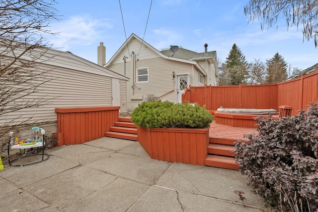 view of patio with a deck, an outdoor hot tub, and fence