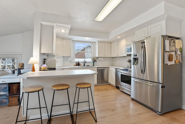 kitchen with a kitchen bar, a sink, tasteful backsplash, appliances with stainless steel finishes, and a peninsula