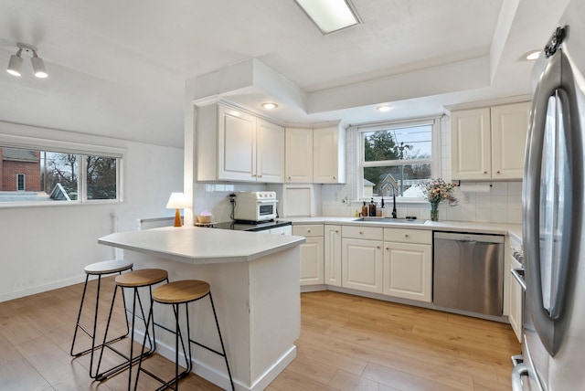 kitchen with a sink, decorative backsplash, light wood-style floors, appliances with stainless steel finishes, and a kitchen breakfast bar