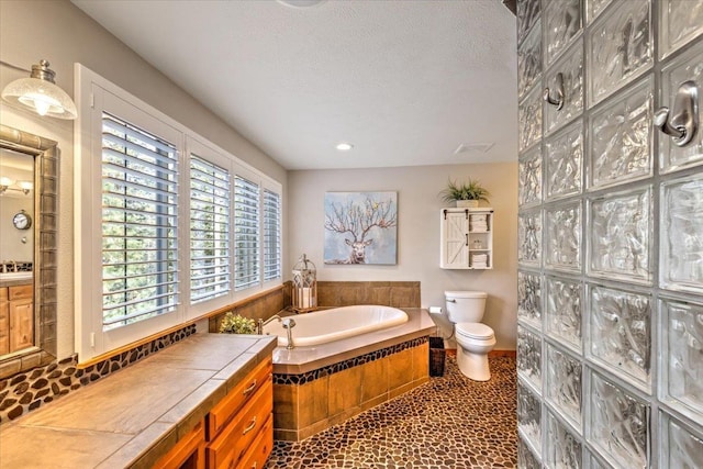 full bathroom featuring a garden tub, toilet, and a textured ceiling