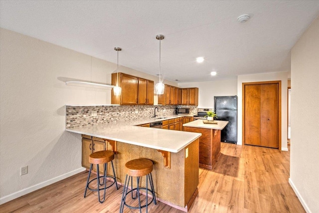 kitchen featuring brown cabinets, a peninsula, black appliances, light countertops, and tasteful backsplash