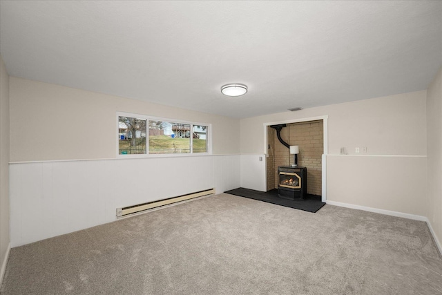 unfurnished living room with a wainscoted wall, a wood stove, carpet, and a baseboard radiator