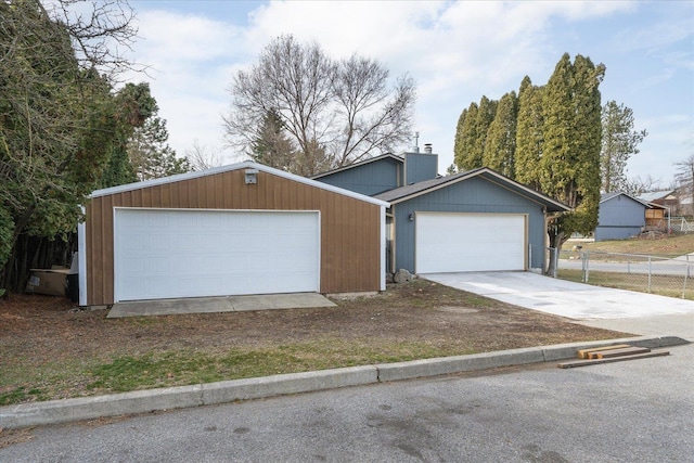 view of front of home featuring an outbuilding, concrete driveway, a chimney, and fence