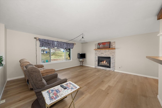 living area with baseboards, light wood-style floors, and a glass covered fireplace