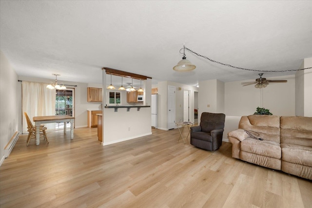 living area featuring light wood finished floors, ceiling fan with notable chandelier, a textured ceiling, and baseboards