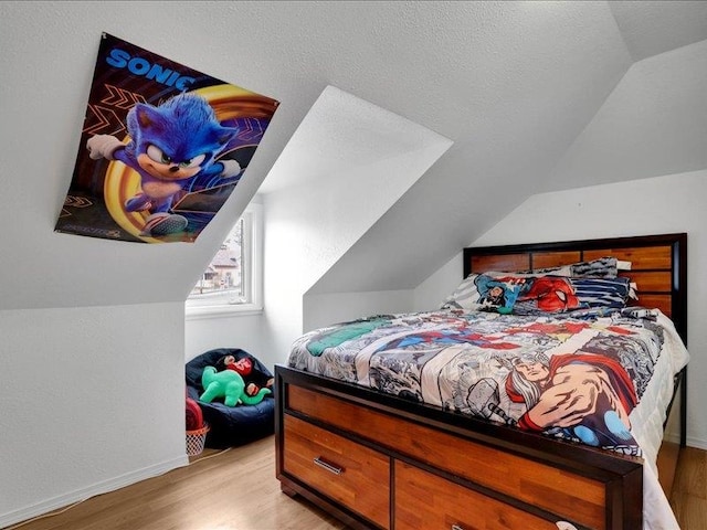 bedroom with vaulted ceiling, light wood-style flooring, baseboards, and a textured ceiling