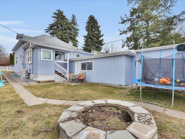 back of house featuring a trampoline, fence, and a yard