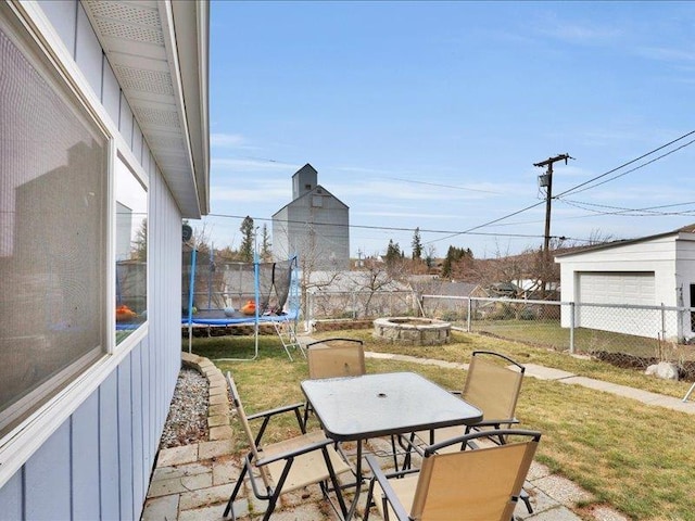 view of patio featuring an outbuilding, fence, an outdoor fire pit, outdoor dining area, and a trampoline