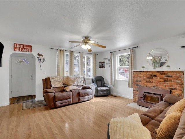 living area featuring baseboards, a textured ceiling, a brick fireplace, and light wood finished floors