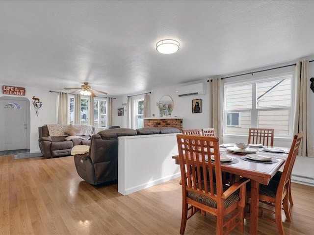 dining space featuring light wood-style flooring, a ceiling fan, and a wall unit AC