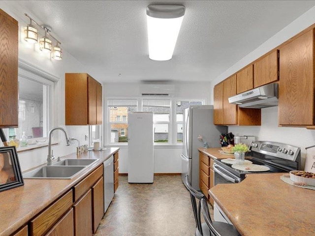 kitchen featuring an AC wall unit, under cabinet range hood, a sink, freestanding refrigerator, and dishwasher