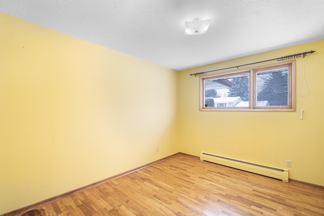 empty room with a baseboard radiator, baseboards, a textured ceiling, and light wood finished floors