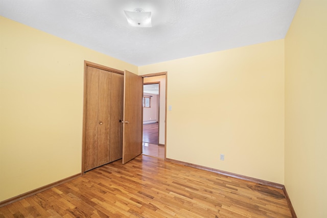 unfurnished room featuring a baseboard heating unit, baseboards, and light wood-style floors