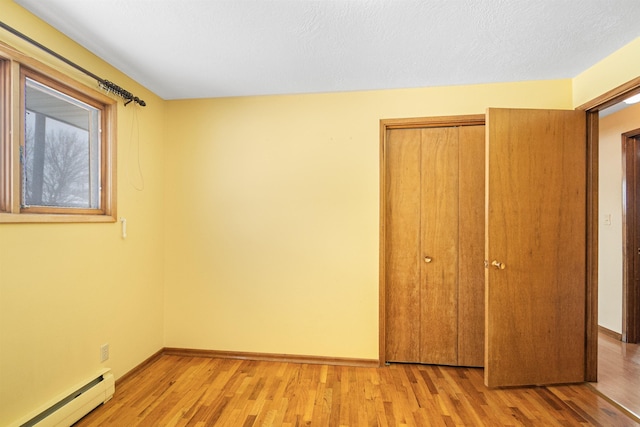 unfurnished bedroom with a baseboard heating unit, baseboards, light wood-type flooring, and a closet