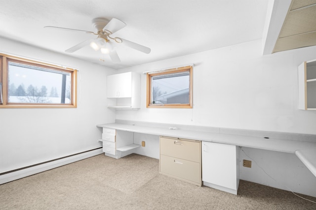 unfurnished office with a baseboard heating unit, a ceiling fan, built in desk, and light carpet