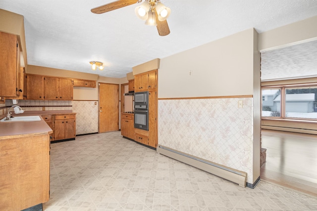 kitchen featuring a sink, a baseboard heating unit, light floors, and wainscoting