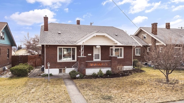 bungalow-style home with brick siding, a front lawn, and fence