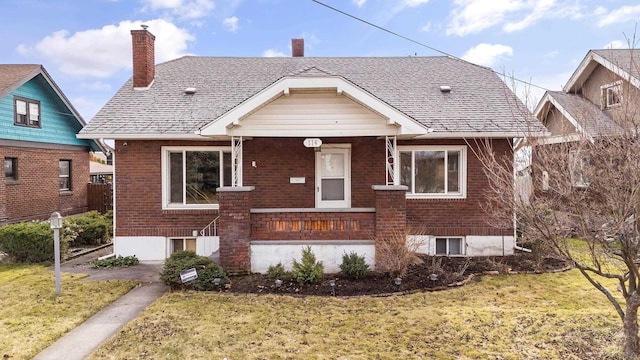 bungalow-style house with brick siding, a front lawn, roof with shingles, covered porch, and a chimney