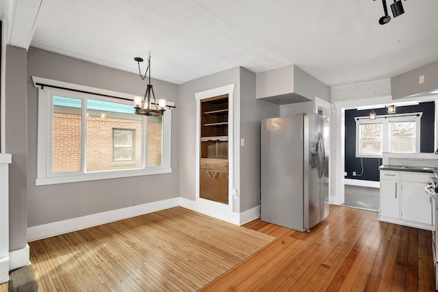 unfurnished dining area featuring light wood-type flooring, baseboards, and an inviting chandelier